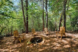 Un bosque con cuatro sillas de madera dispuestas alrededor de una fogata.