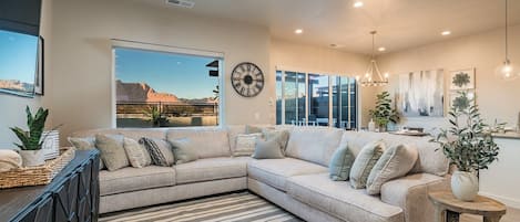 A modern living room with a large sectional sofa, a dining area, and a view of the outdoors.