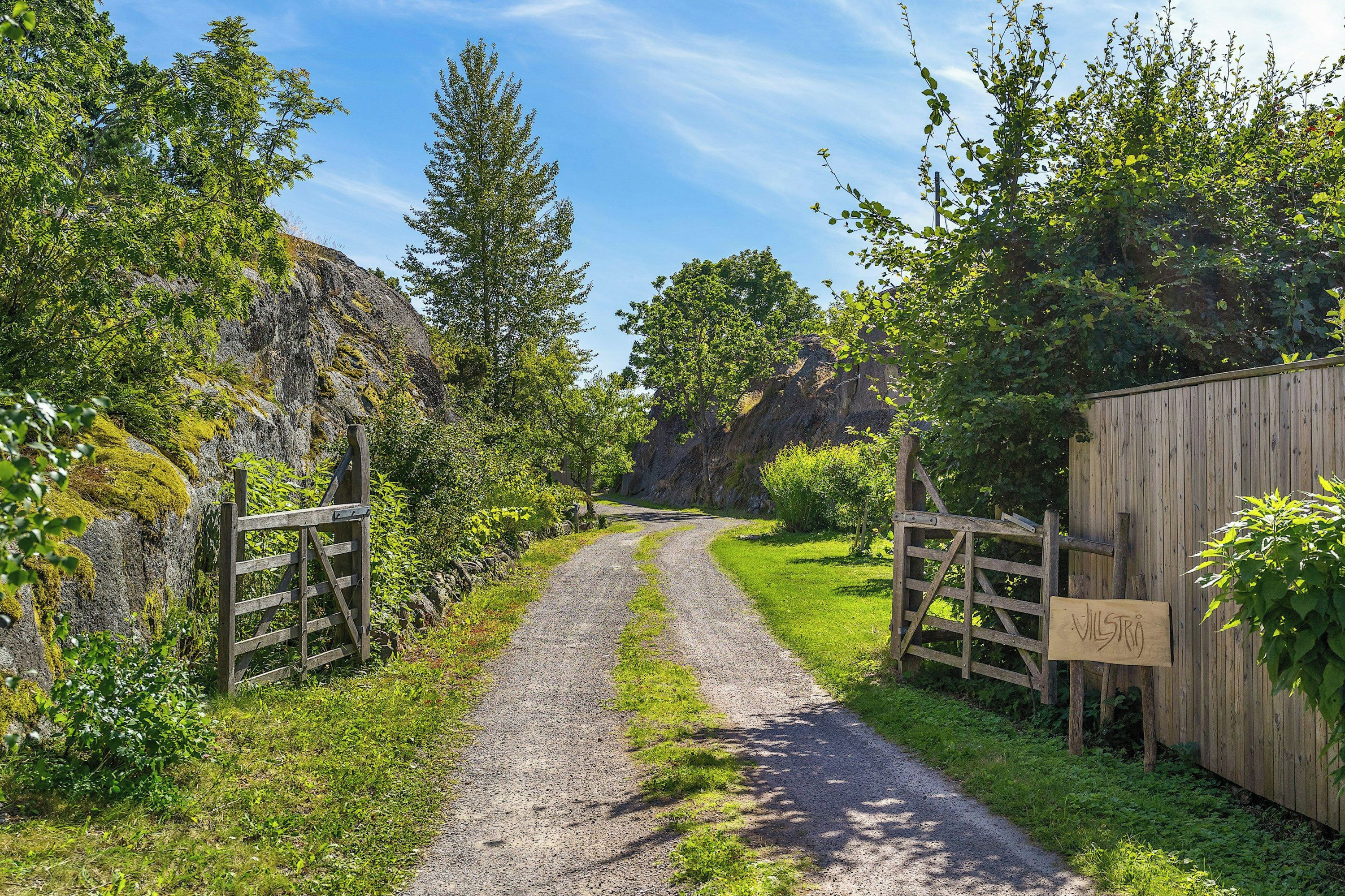 Un sendero de grava que atraviesa un paisaje rural con portones y una valla de madera.