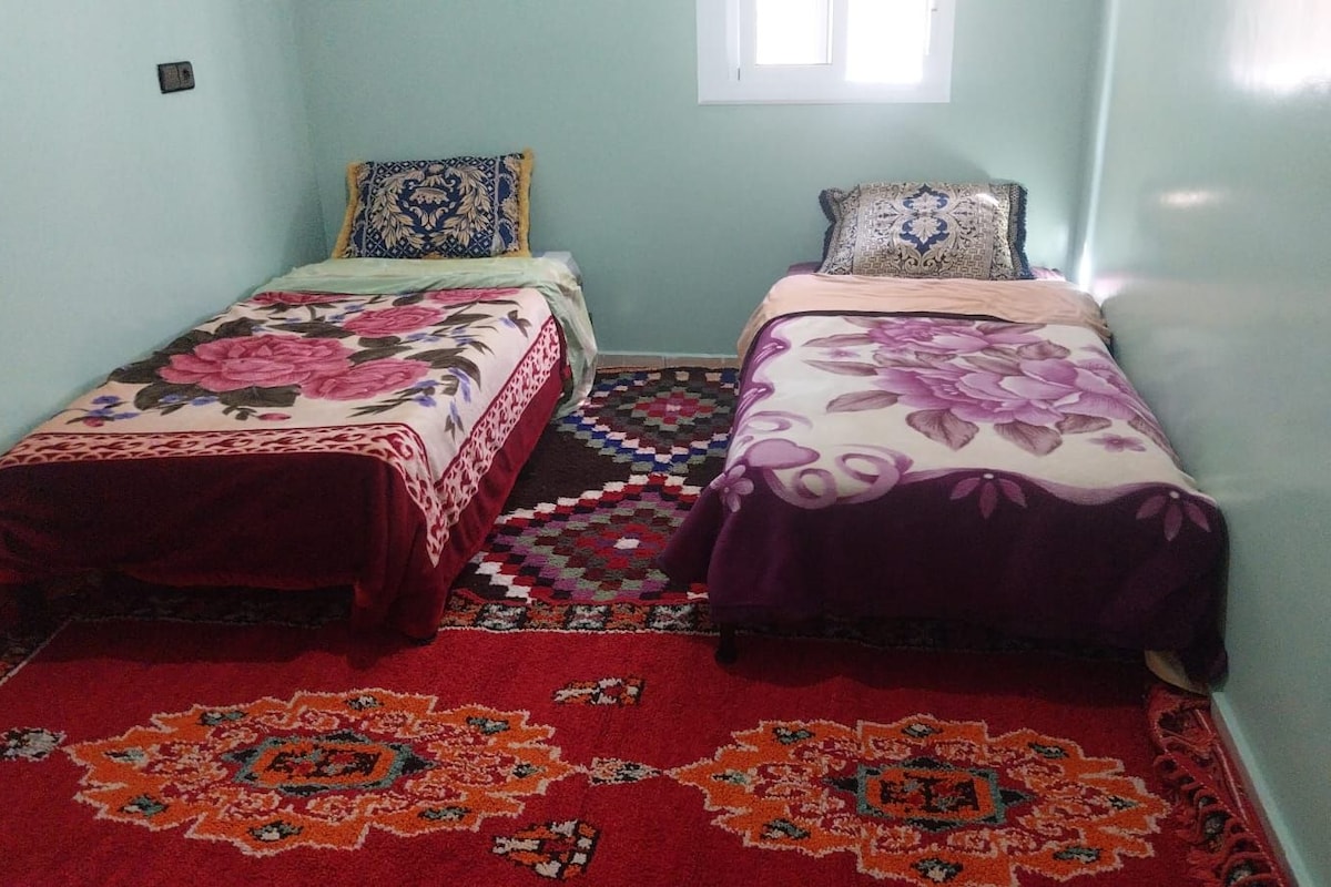 Habitación con dos camas, cada una con cubrecama floral, un tapete estampado y una ventana con luz natural.