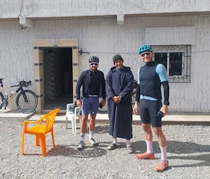Three people standing in front of a building with a bicycle and a chair. - Berber Family Guesthouse (Tilmi)