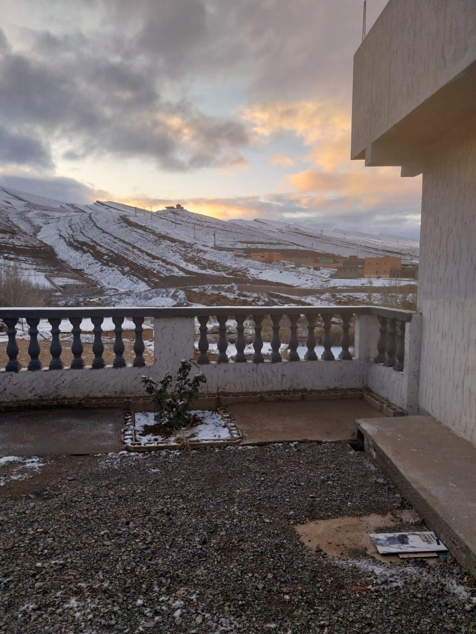 A balcony with a view of snow-covered mountains and a cloudy sky.
