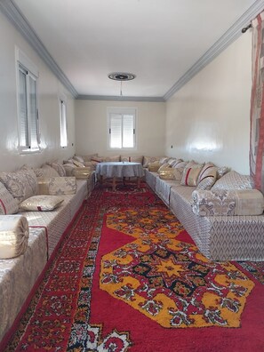 A room with a sofa set, a dining table, and a patterned carpet.