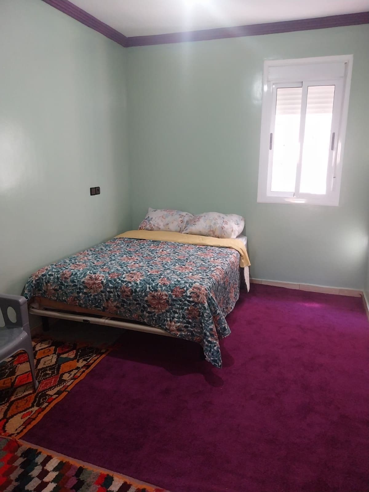 A bedroom with a bed, a window, and a carpeted floor.