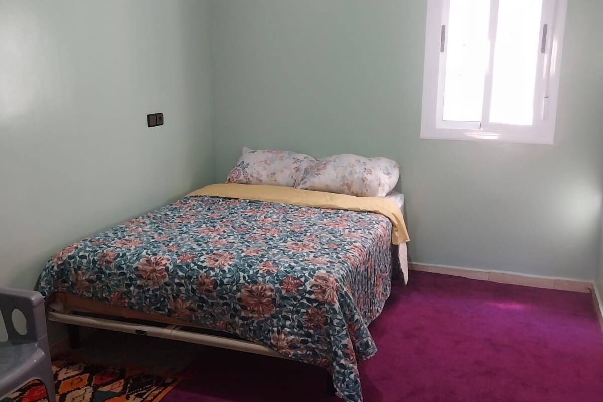 A bedroom with a bed, a window, and a carpeted floor.