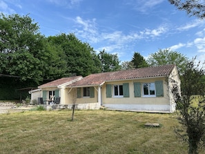 A two-story house with a tiled roof, green shutters, and a grassy yard.