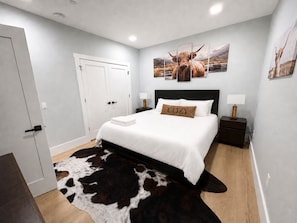 A bedroom with a bed, a cow-themed wall art, a cow-patterned rug, and a nightstand with a lamp. - New Spacious Mountain Modern Home • 5 bedroom/5 Bath • Walk Wisp • Sauna/Hot Tub (McHenry)