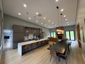 A modern kitchen with a central island, bar stools, pendant lighting, and a dining area with a long table and chairs. - New Spacious Mountain Modern Home • 5 bedroom/5 Bath • Walk Wisp • Sauna/Hot Tub (McHenry)