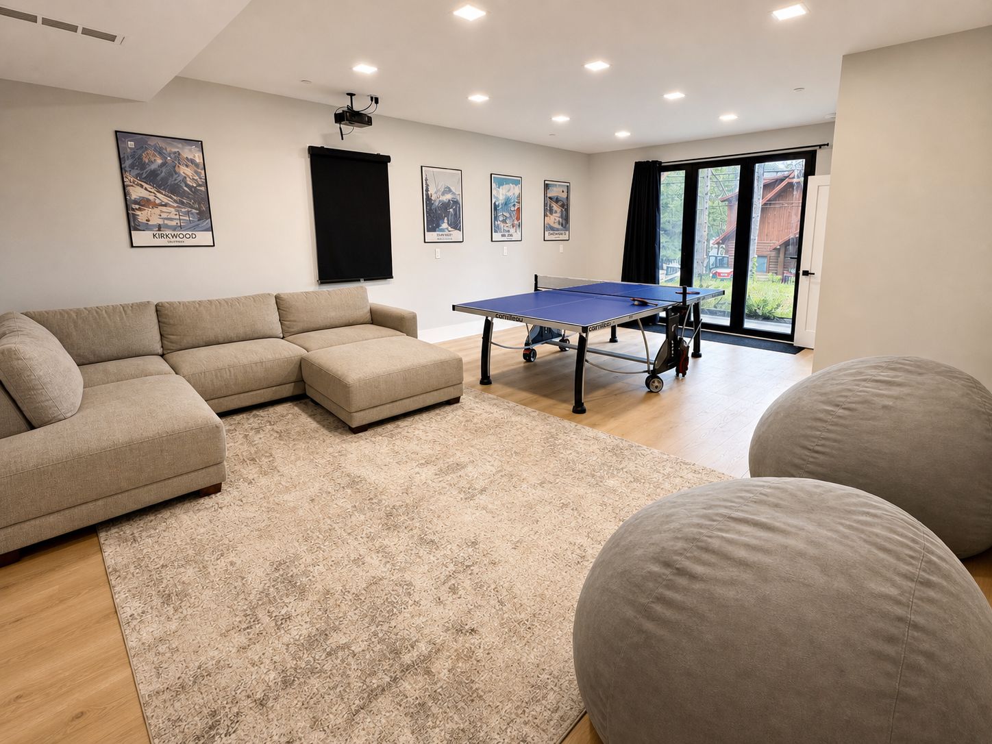 A modern living room with a sectional sofa, a ping pong table, and a large window with a view.