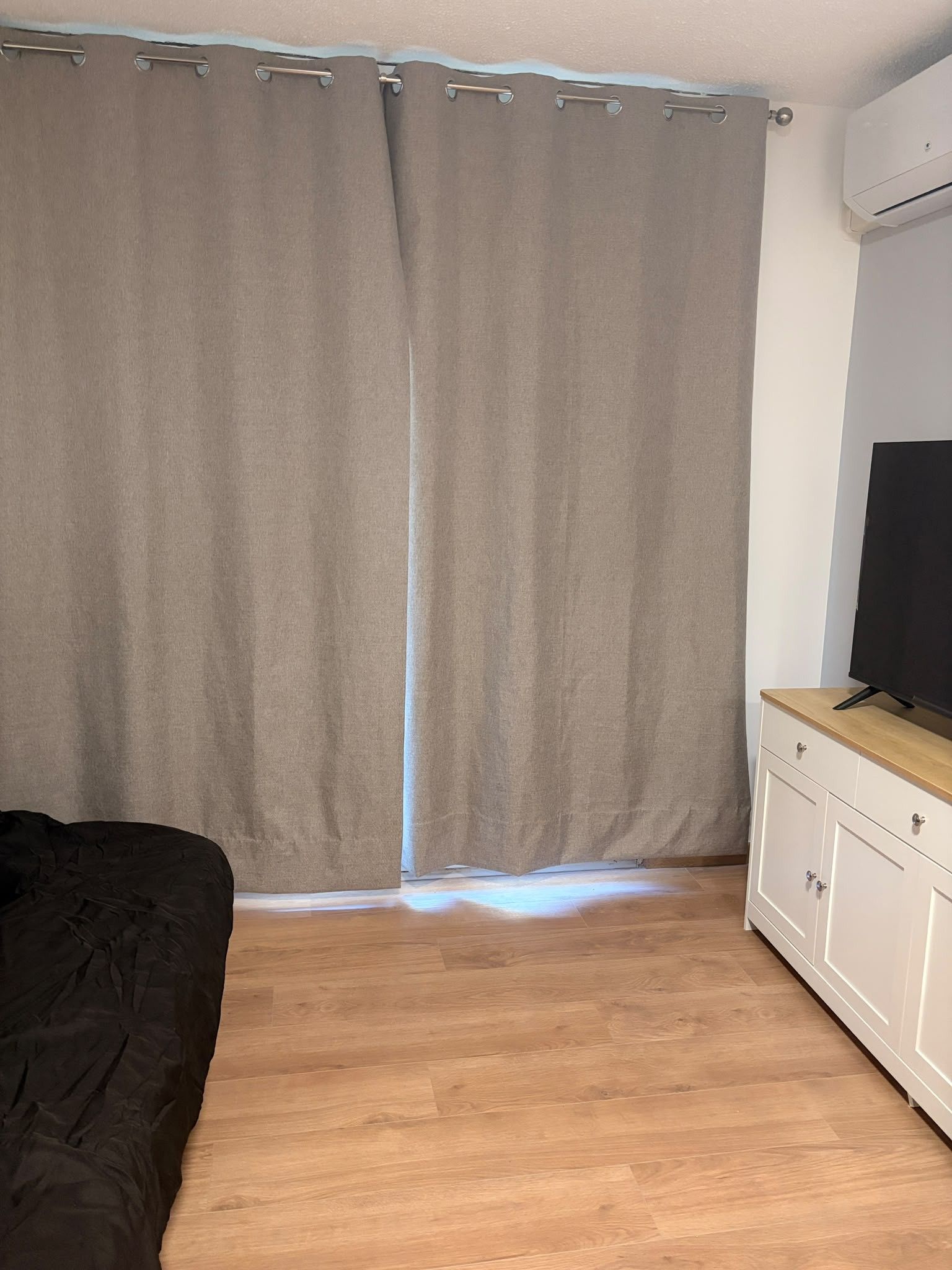 A room with a bed, a TV on a wooden cabinet, and a large window with curtains.