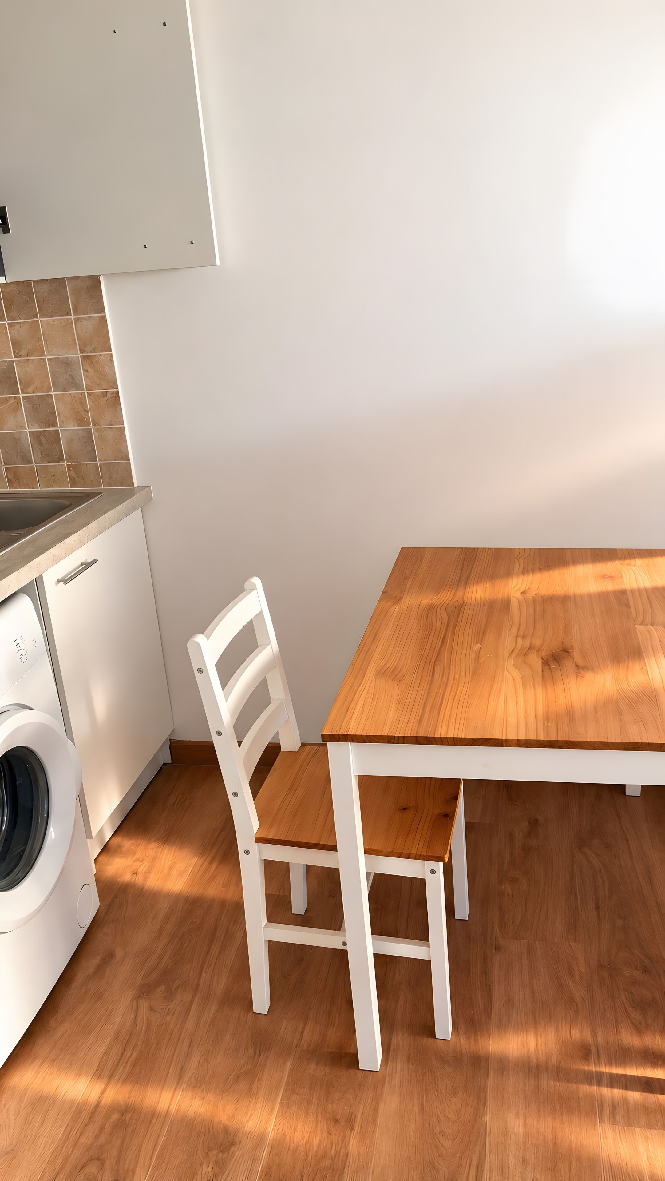 Eine kleine Küche mit Waschmaschine, einem Holztisch und einem weißen Stuhl.
