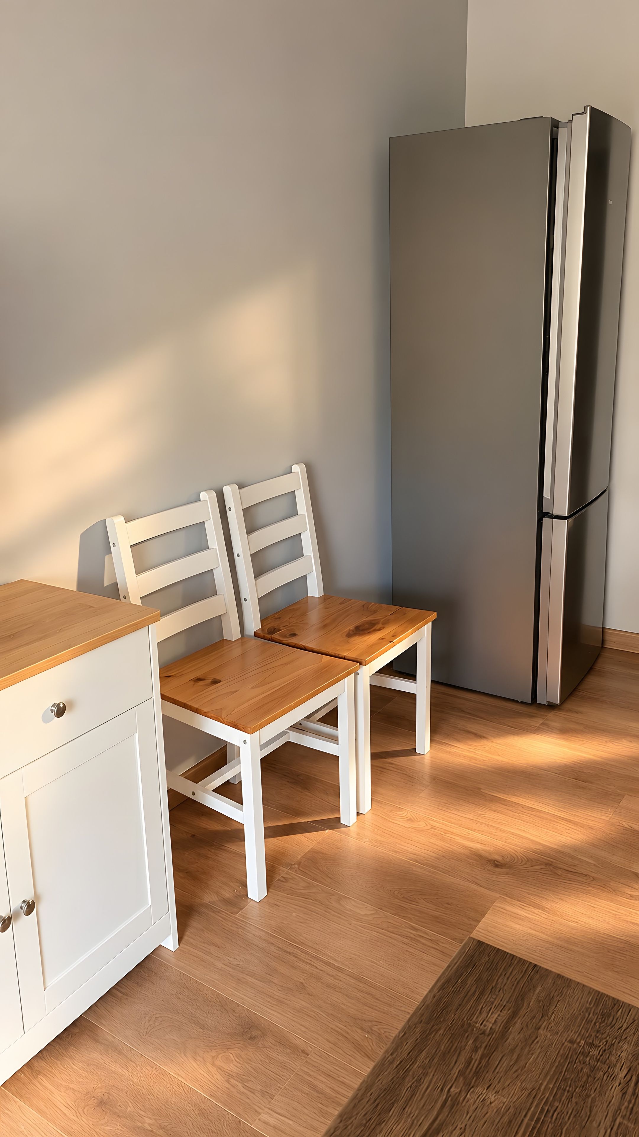 Eine Küche mit einem weißen Schrank, einem Holztisch, zwei Stühlen und einem Edelstahlkühlschrank.