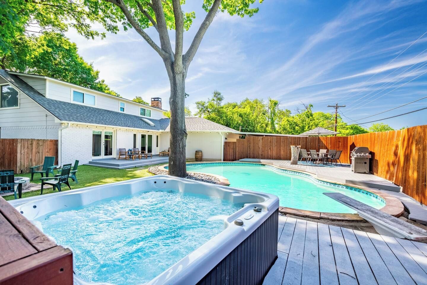 A backyard with a hot tub, a swimming pool, and a wooden deck.