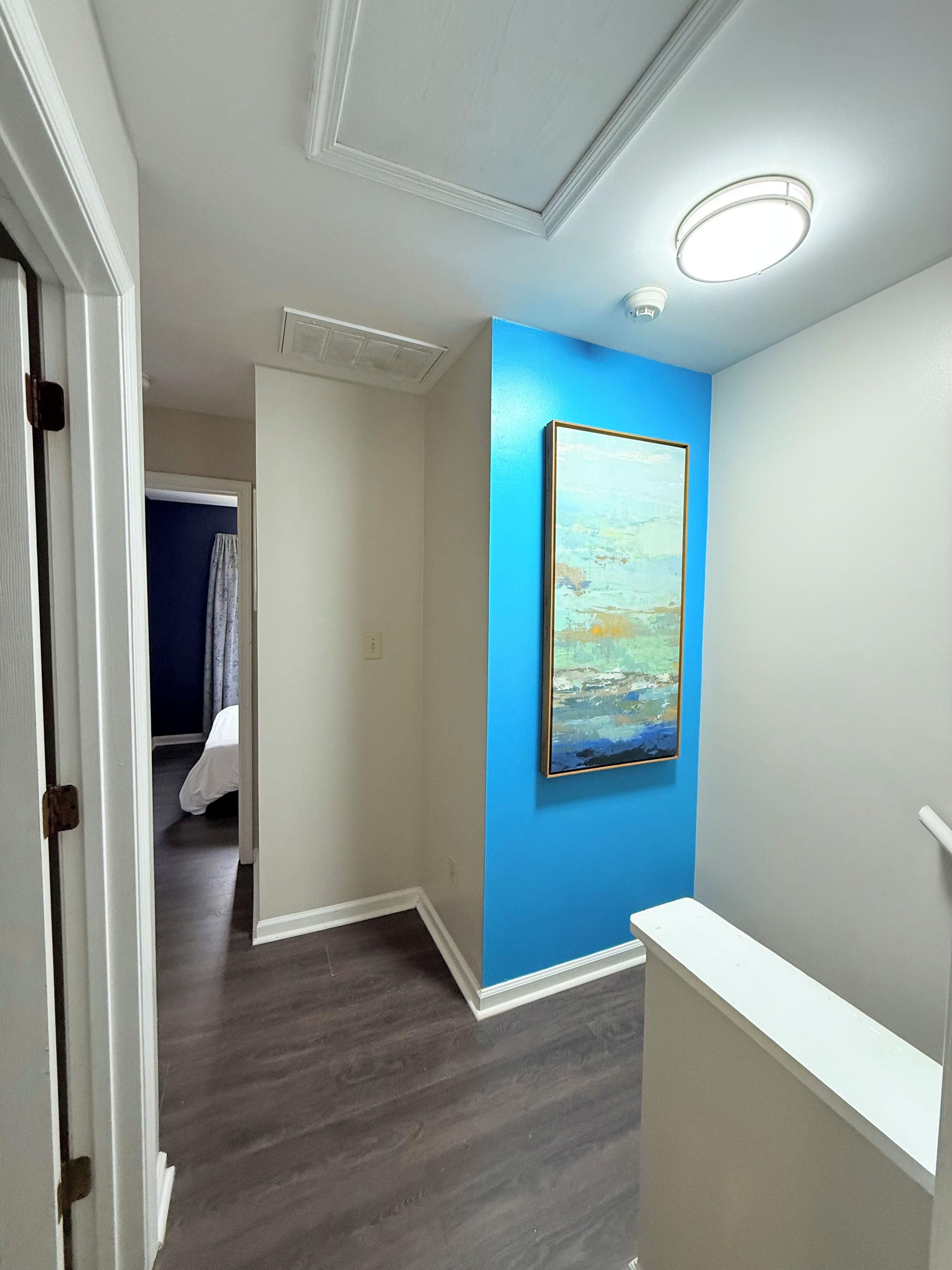 Un couloir avec un mur d’accent bleu, un tableau et un luminaire au plafond.