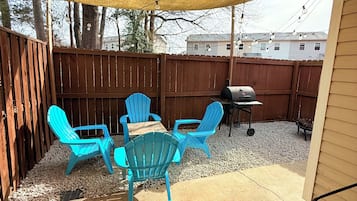 Un patio con una mesa, cuatro sillas, una parrilla y una valla de madera.