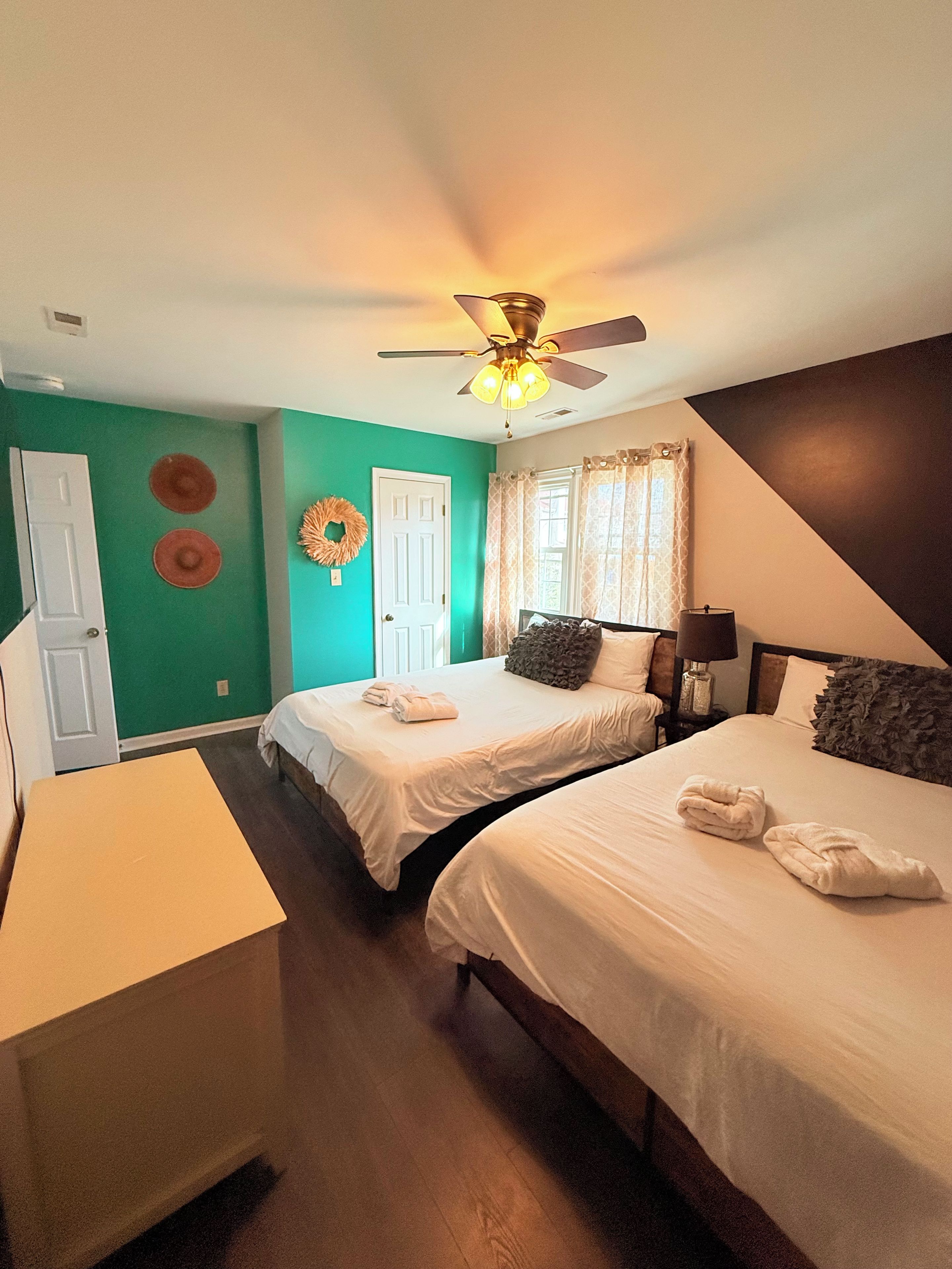 Une chambre d’hôtel avec deux lits, un ventilateur de plafond, un bureau et une fenêtre avec des rideaux.