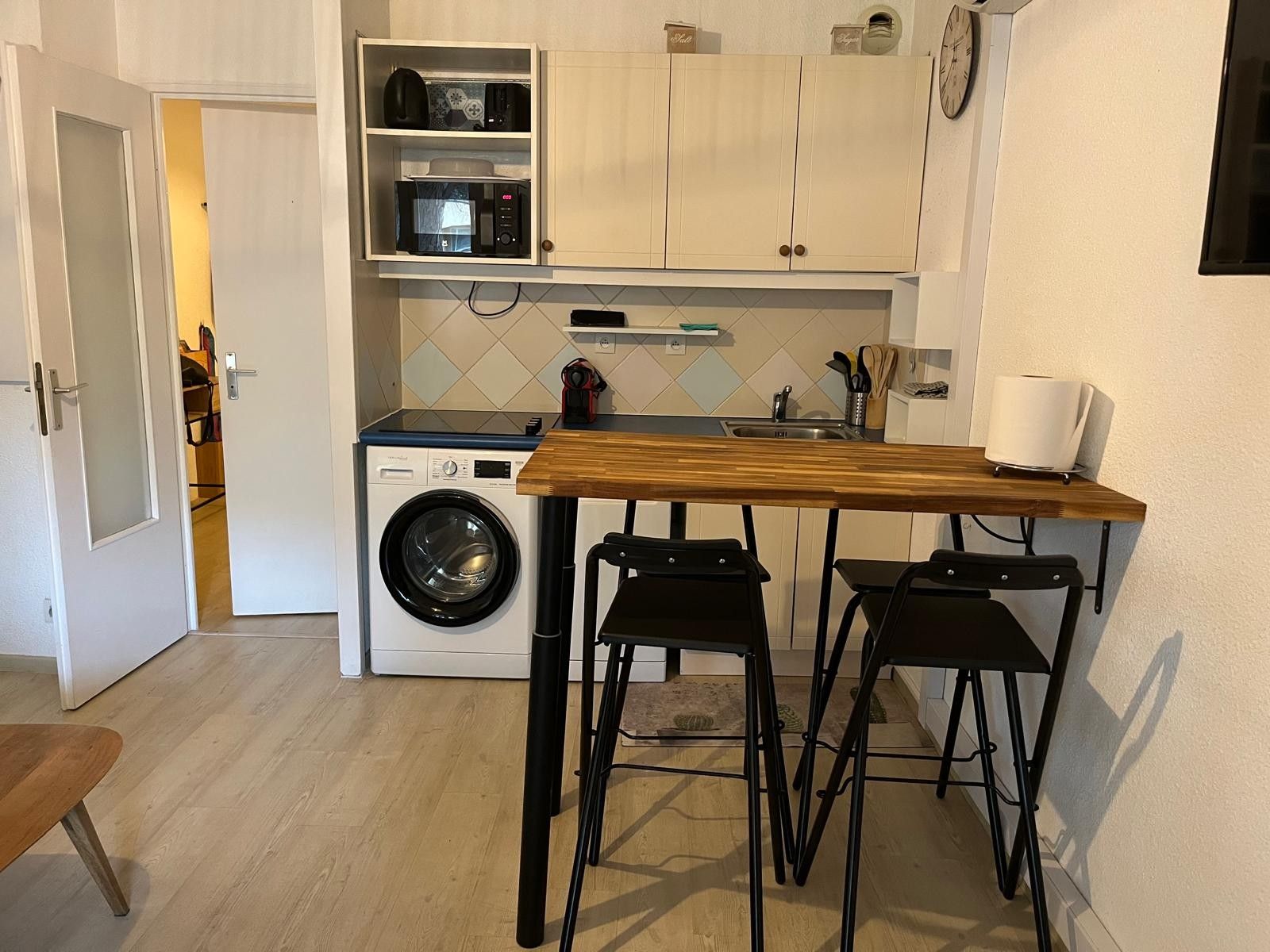 Eine kleine Küche mit Waschmaschine, einem Holztisch und zwei Barhocker.