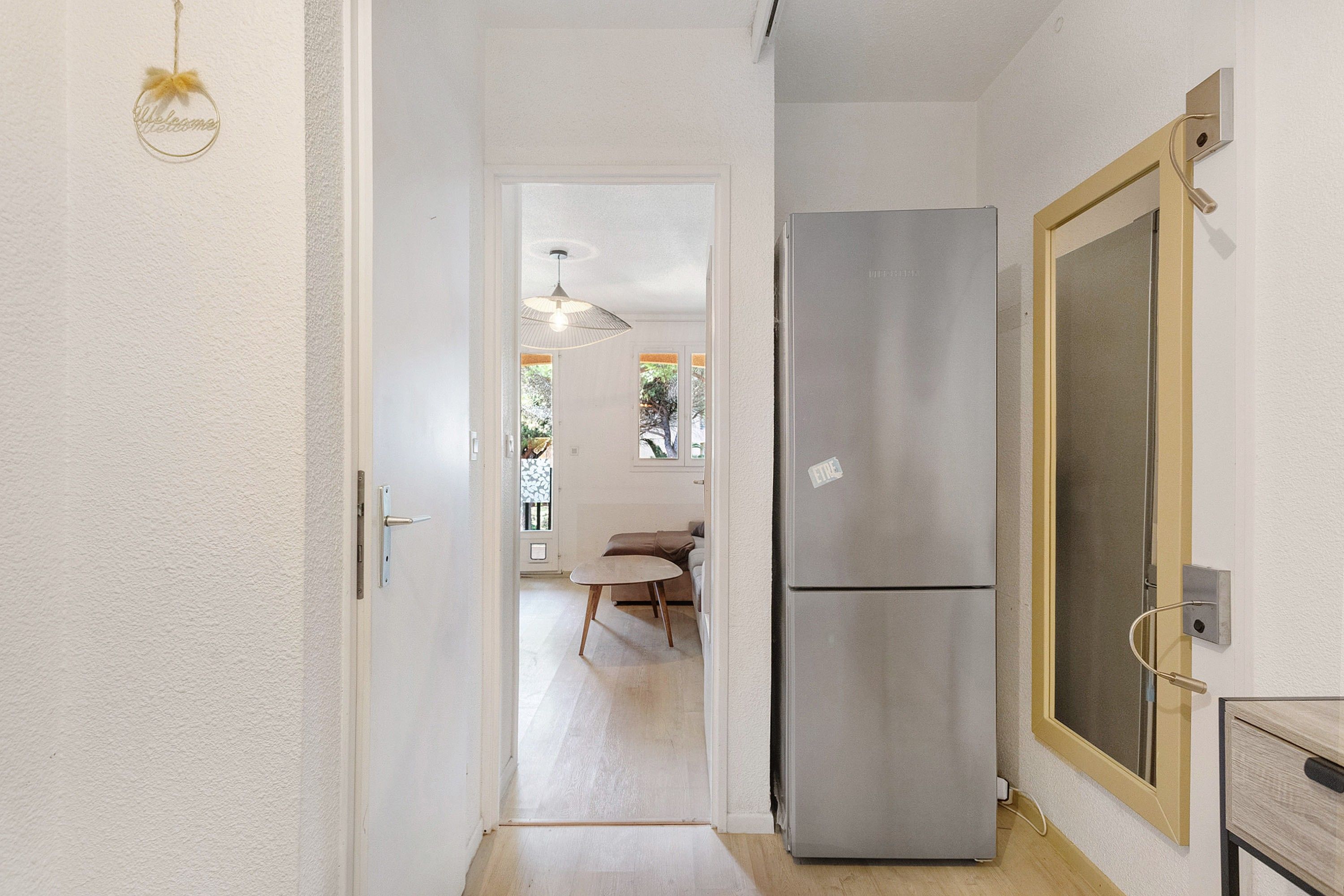 Un couloir avec une porte donnant sur un coin repas, un réfrigérateur et un luminaire.