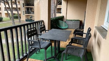 Un balcone con tavolo e sedie, una sedia verde e un armadietto grigio.