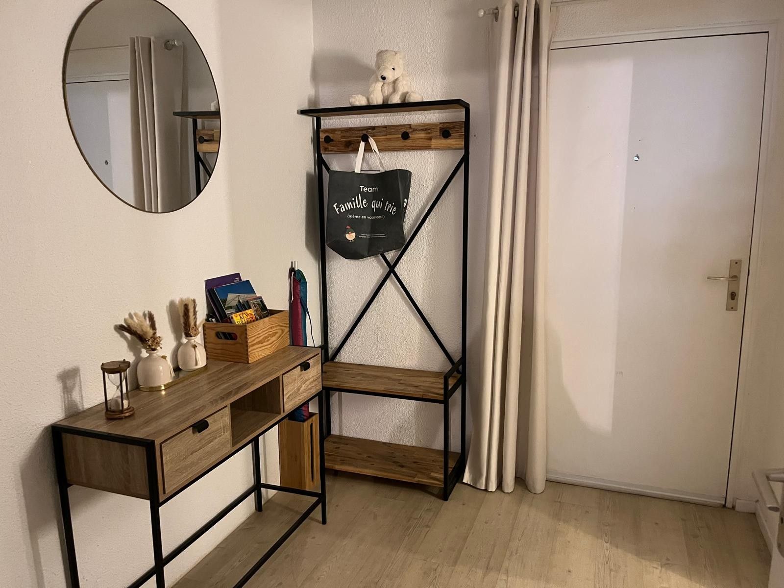 Ein Zimmer mit einem Holztisch, einem Spiegel, einem Regal mit einem Teddybären und einer Tür.