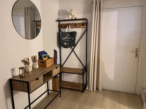 Ein Zimmer mit einem Holztisch, einem Spiegel, einem Regal mit einem Teddybären und einer Tür.