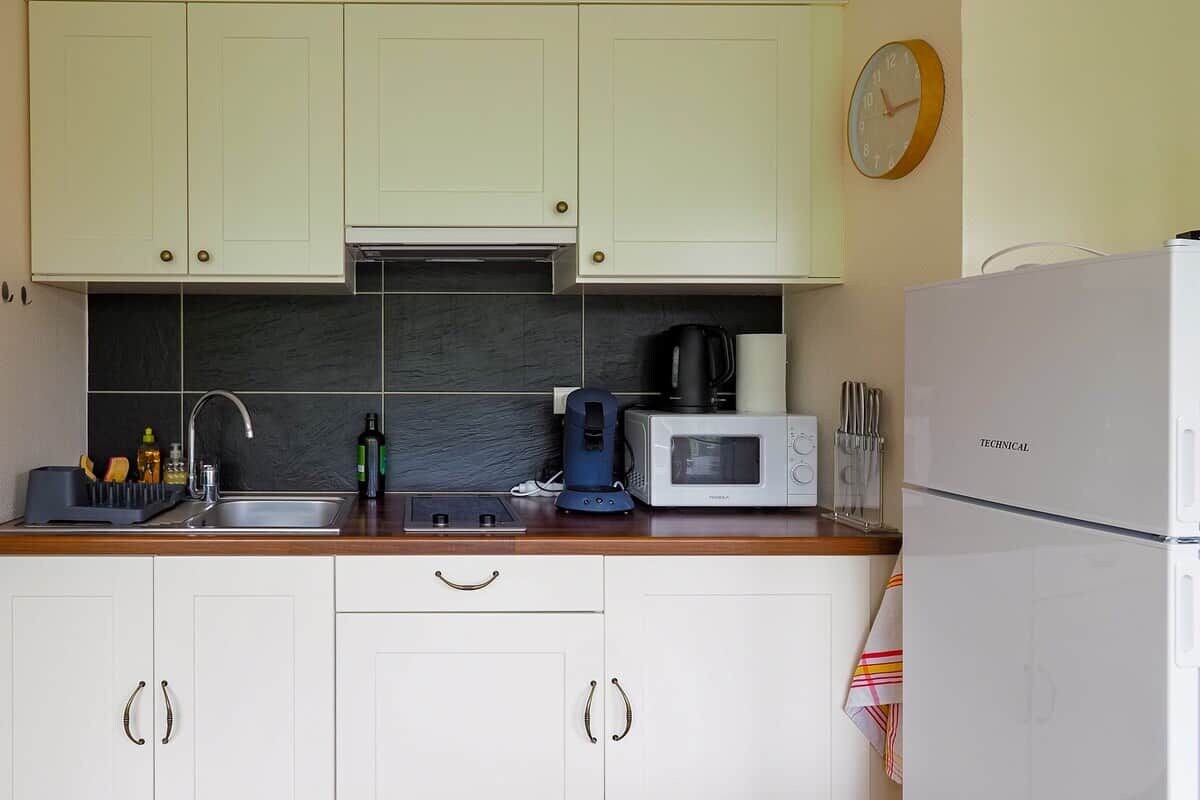 A kitchen with white cabinets, a microwave, a coffee maker, and a refrigerator.