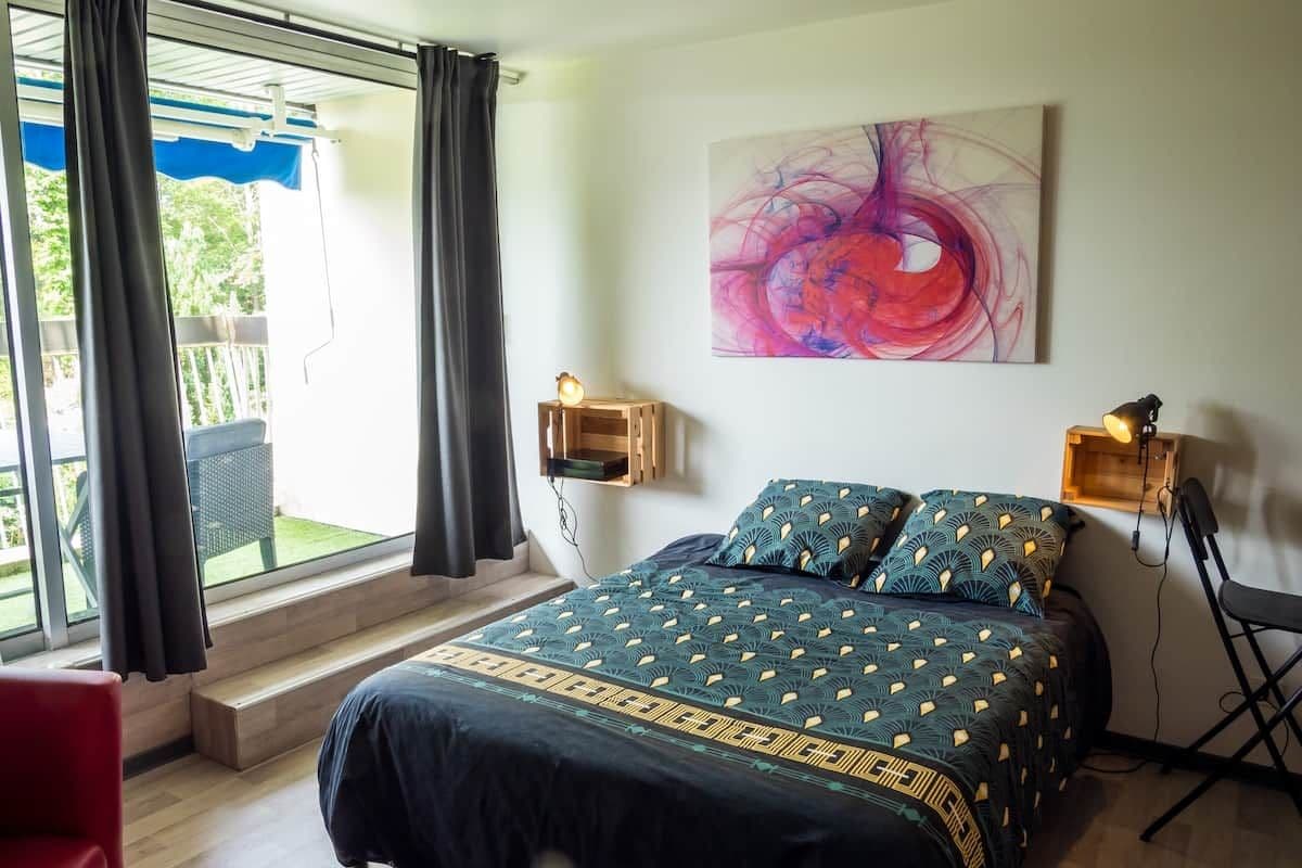 A bedroom with a bed, a chair, a desk, a window with curtains, and a painting on the wall.