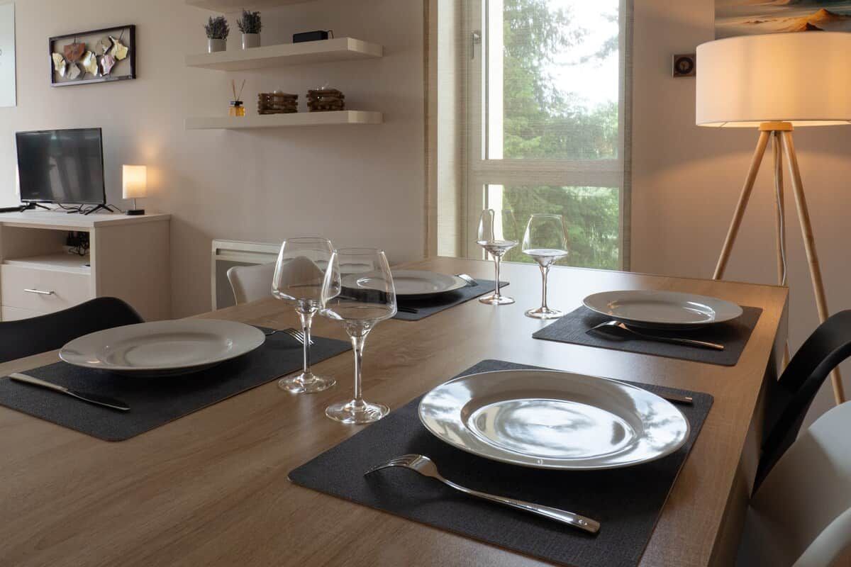 A dining table set with plates, glasses, and cutlery, with a television and shelves in the background.