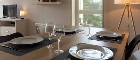 A dining table set with plates, glasses, and cutlery, with a television and shelves in the background.