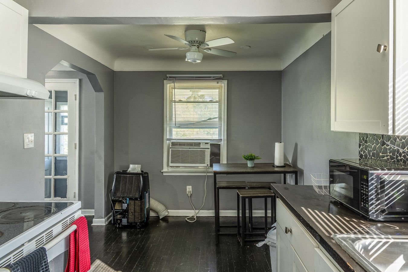 A compact kitchen with a stove, microwave, and a ceiling fan.
