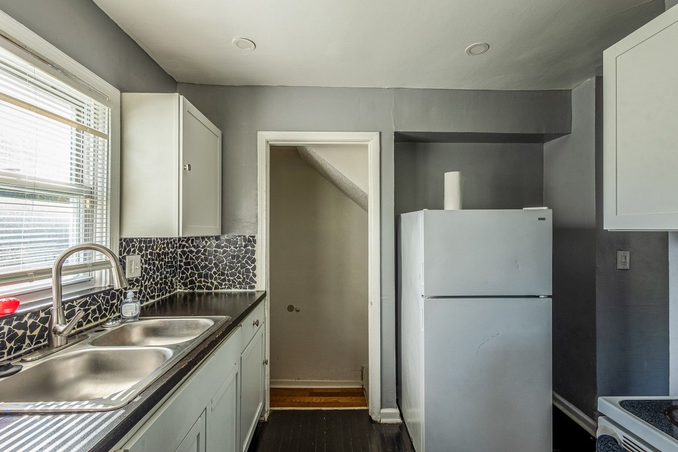 A compact kitchen with a double sink, a refrigerator, and a tiled backsplash.