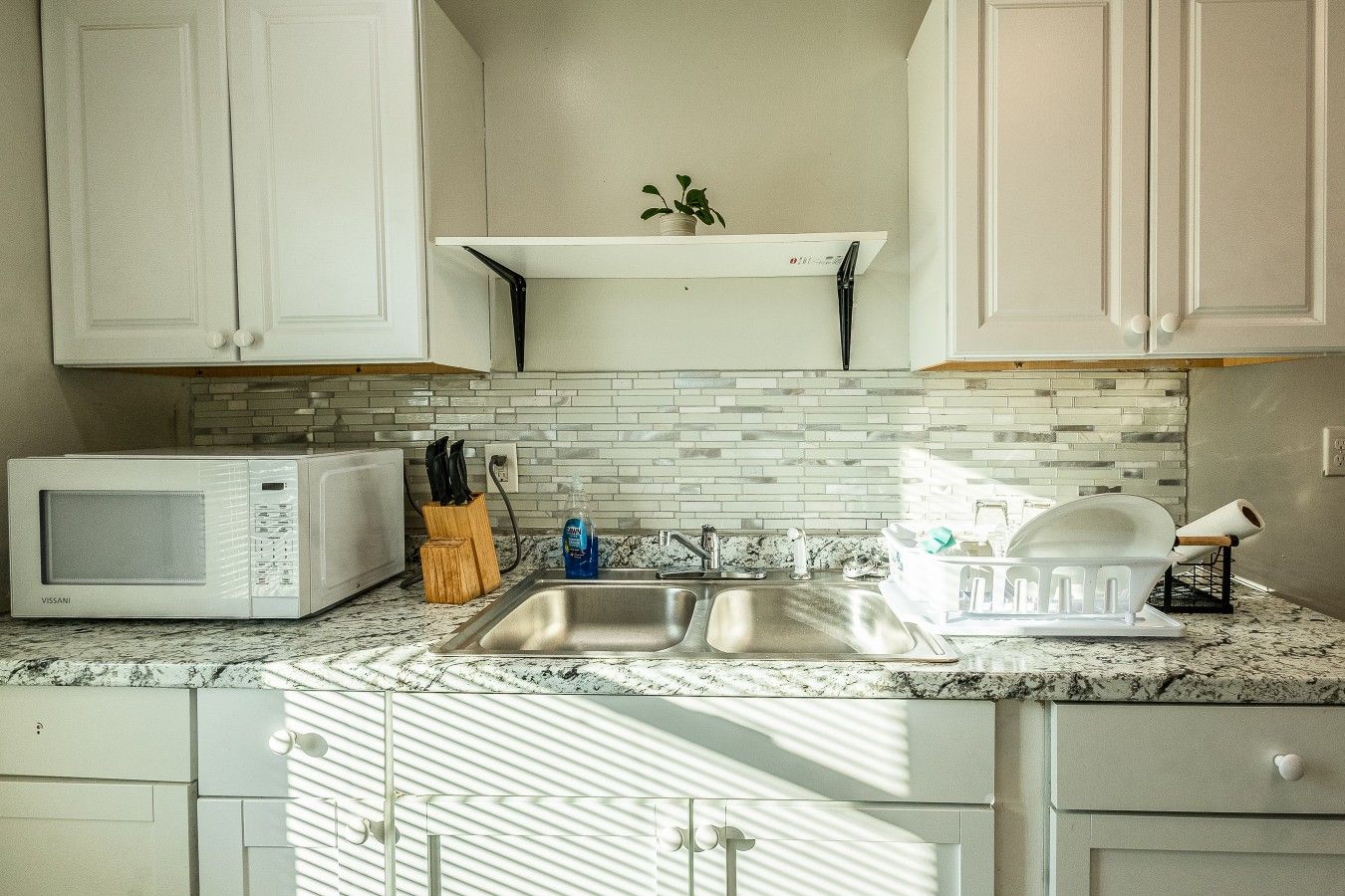 A kitchen with white cabinets, a microwave, a sink, and a dish rack.