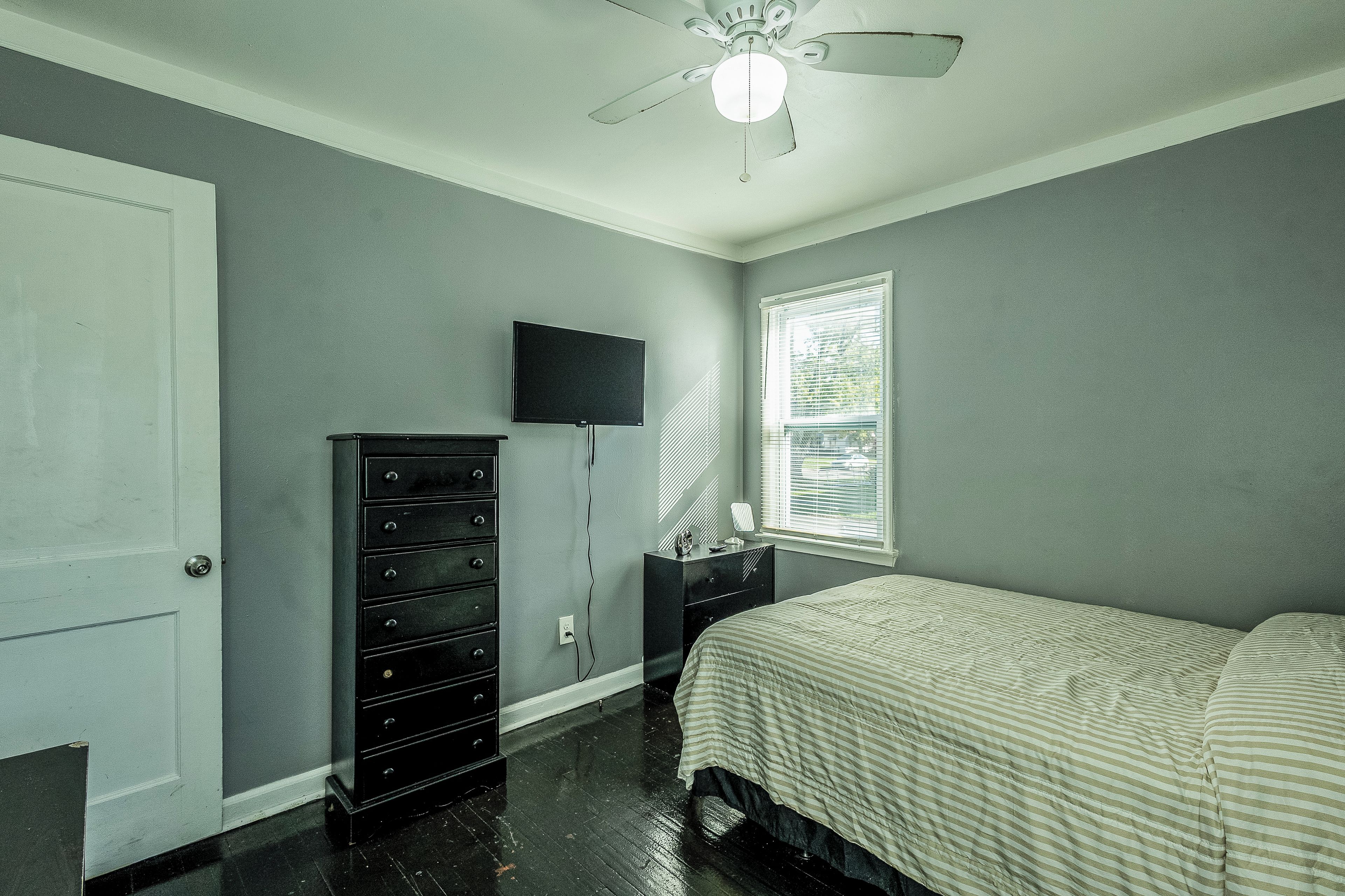 A bedroom with a bed, dresser, television, and a ceiling fan.