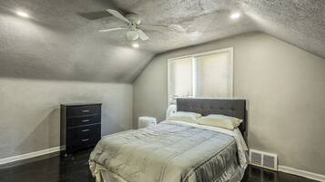 A bedroom with a sloped ceiling, a bed with a headboard, a dresser, and a window with blinds.