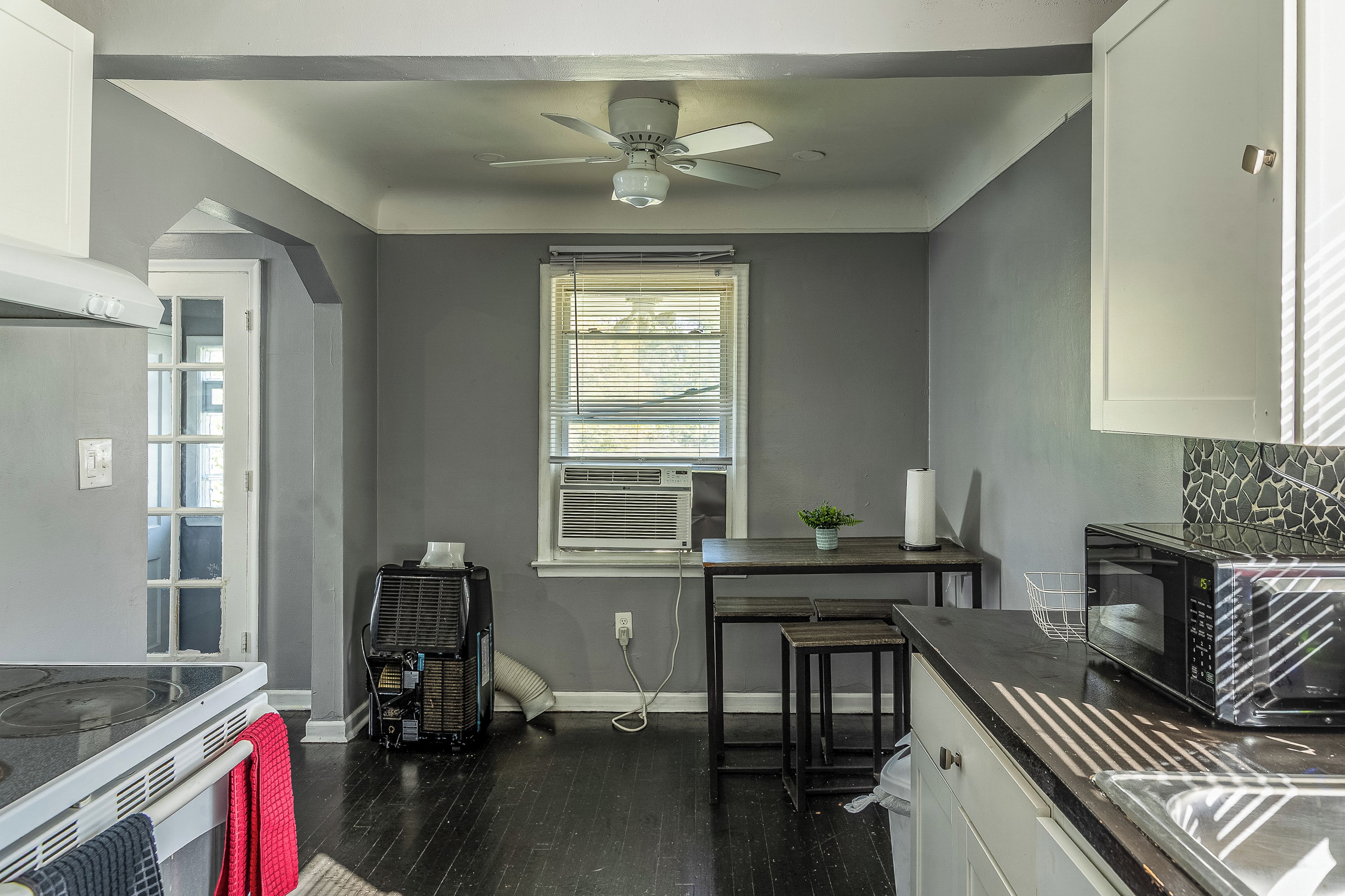 A compact kitchen with a ceiling fan, a window with blinds, a microwave, and a stove.