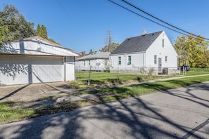 A residential area with a white garage, a detached house with a sloped roof, and a chain-link fence. - Heyden House - Detroit 3BR Stay (Detroit)