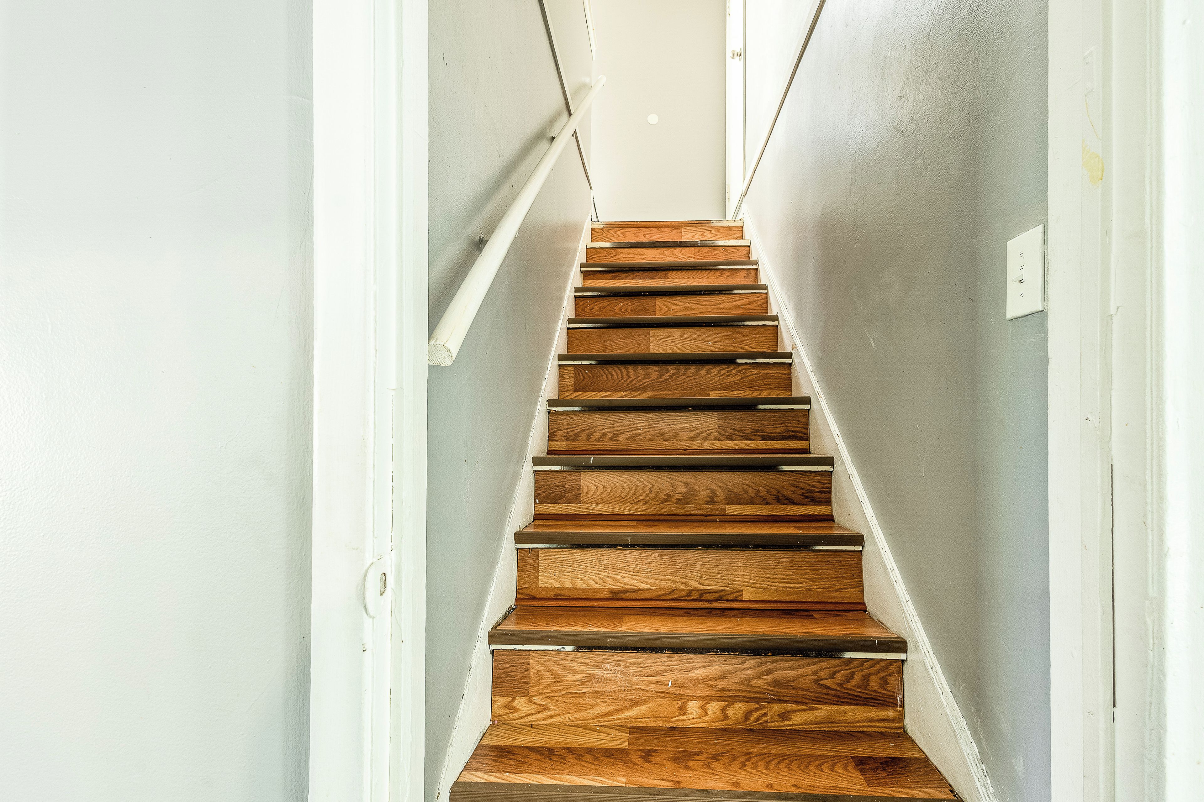 A wooden staircase with white walls and a light-colored floor.
