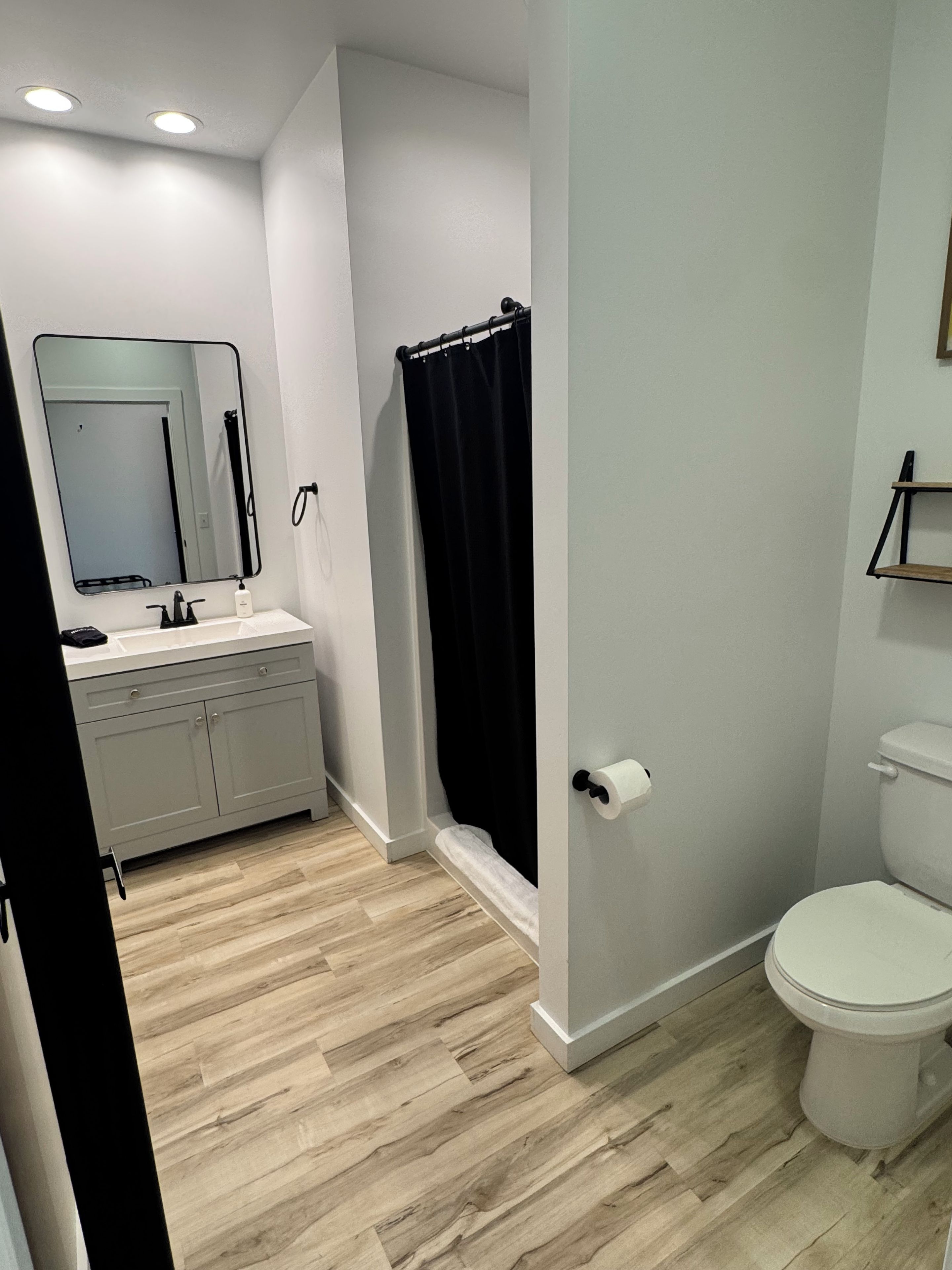 A bathroom with a toilet, a sink with a mirror, a shower curtain, and a toilet paper holder.