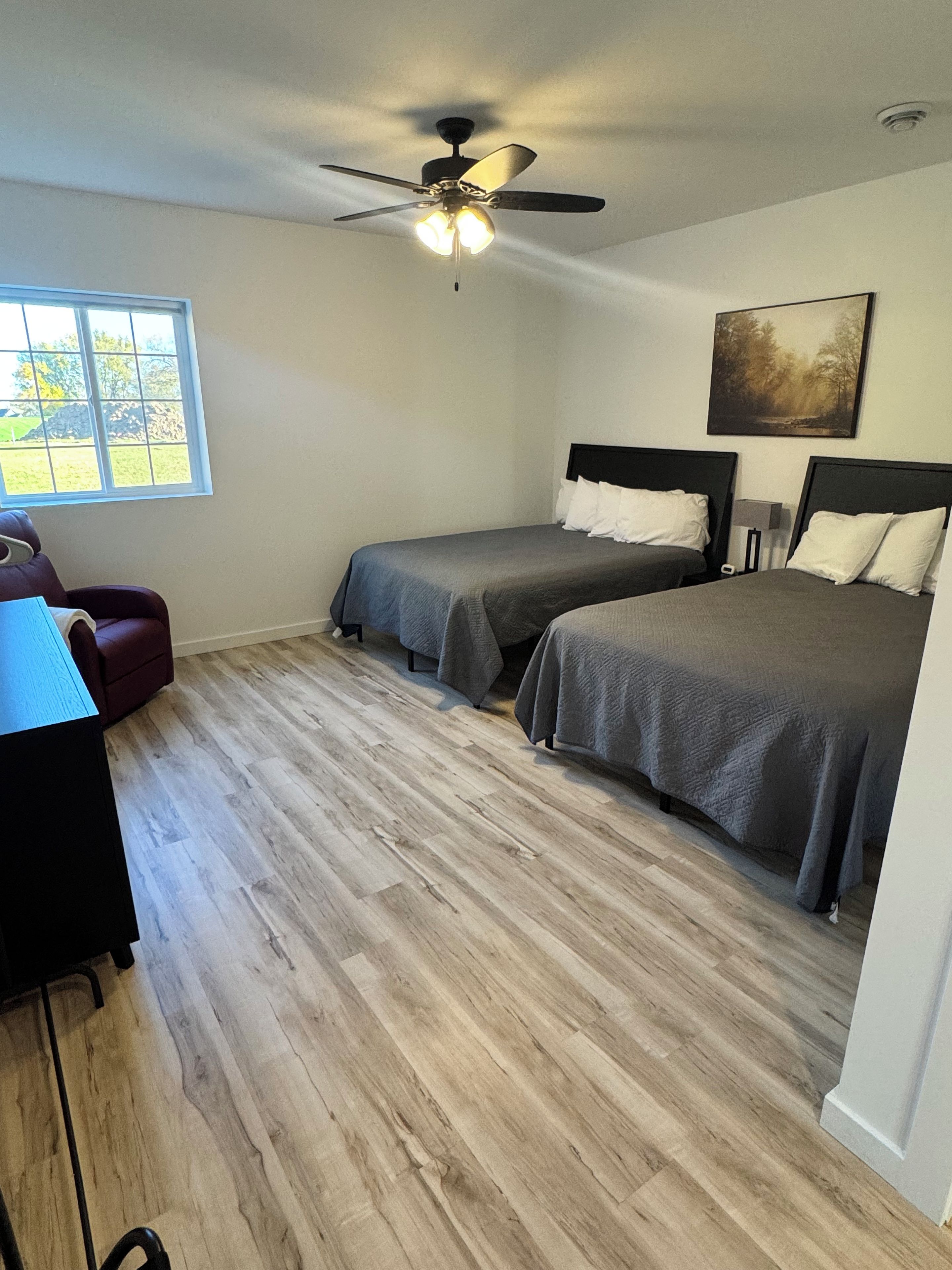 A bedroom with two beds, a ceiling fan, a window, and a desk.