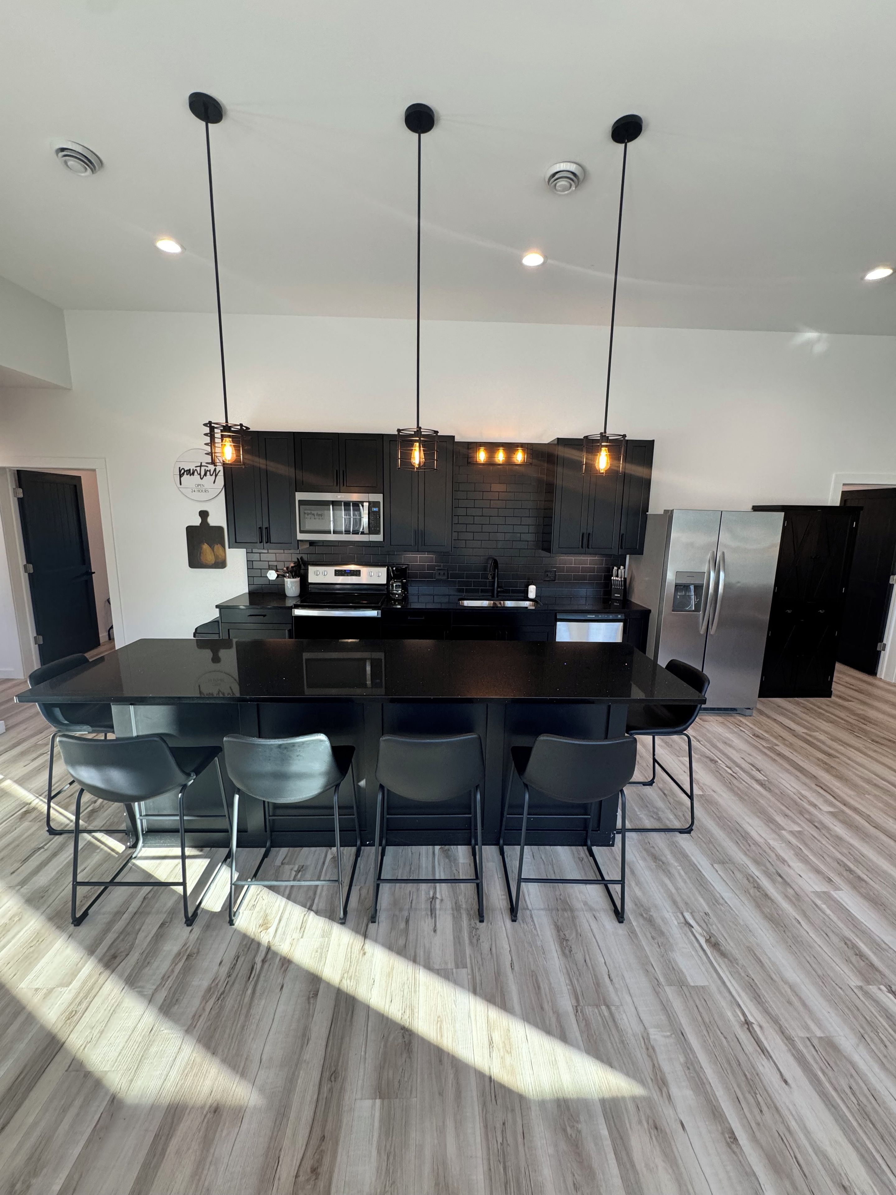 A modern kitchen with a central island, black cabinetry, stainless steel appliances, and pendant lighting.