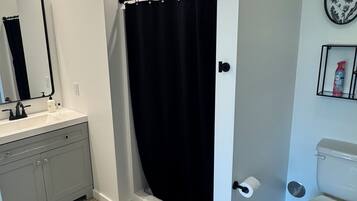 A bathroom with a shower curtain, toilet, sink, and mirror.