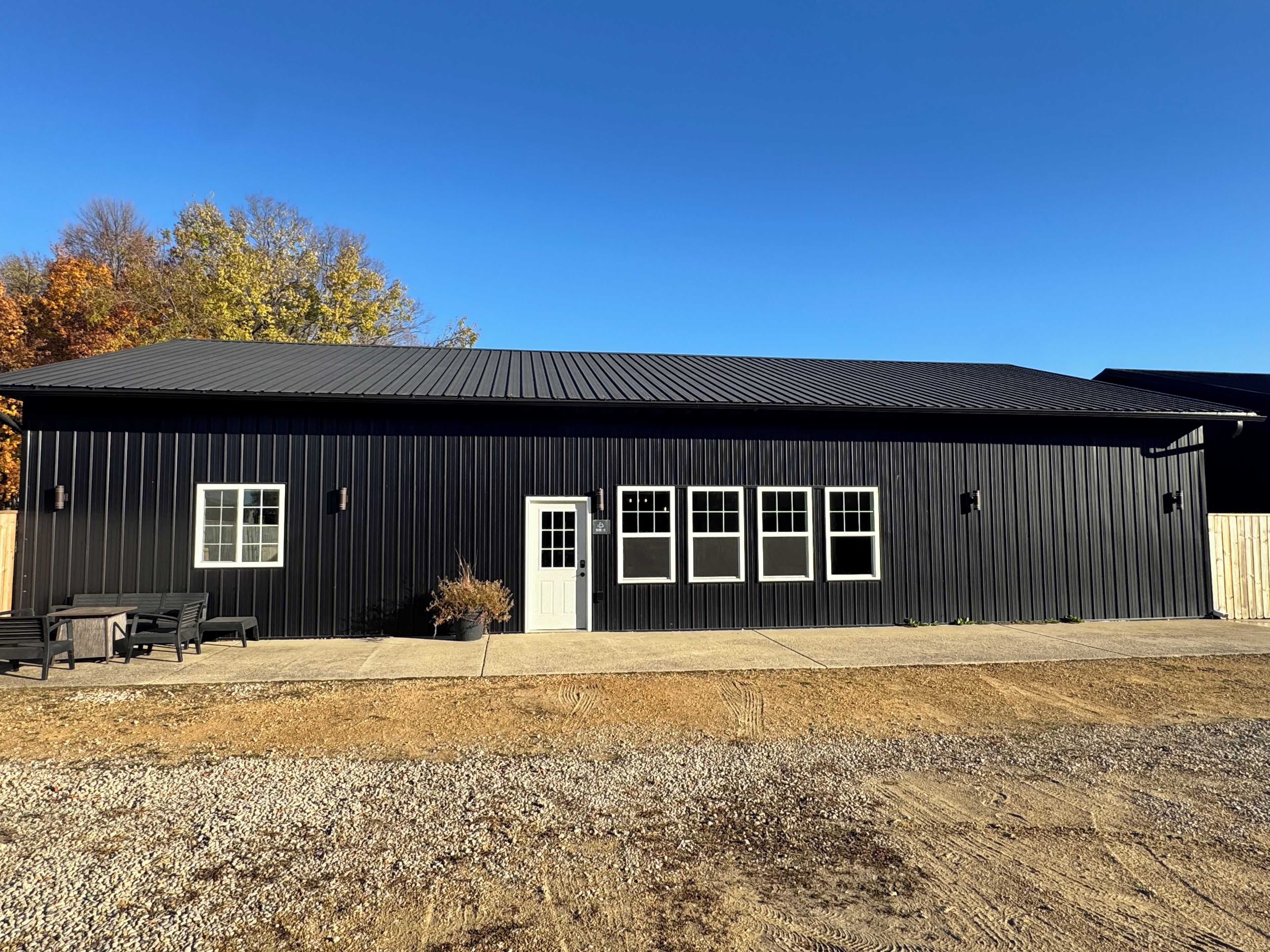 A black metal building with a door, windows, and a patio area with seating.