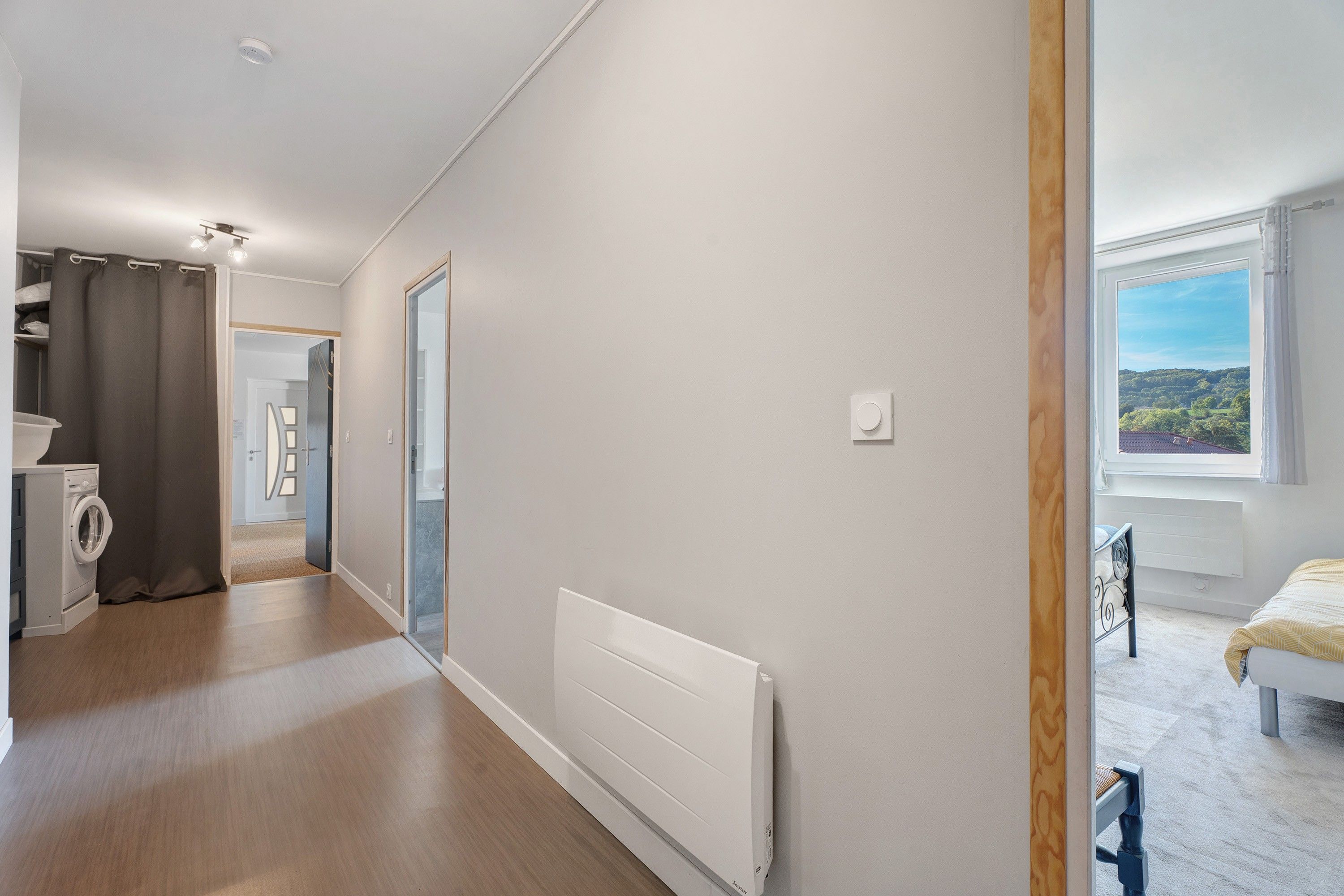 A modern apartment with a laundry area, a radiator, and a view of the outdoors.