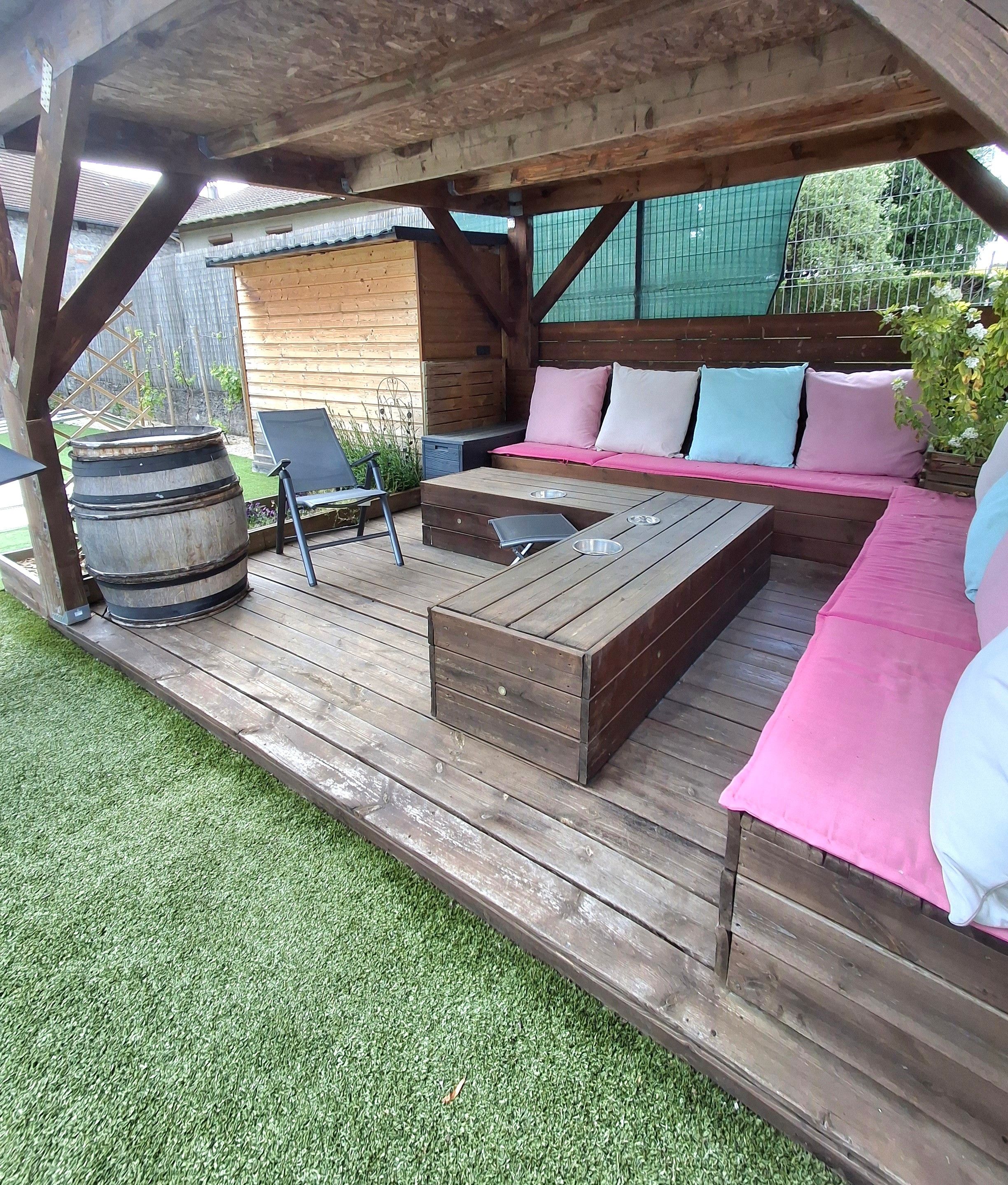 Una terraza de madera con una zona de estar integrada, un barril y una silla metálica.