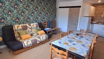 Una sala de estar con un papel tapiz decorativo, un sofá, una mesa de comedor con sillas y una cocina con armarios y un refrigerador.