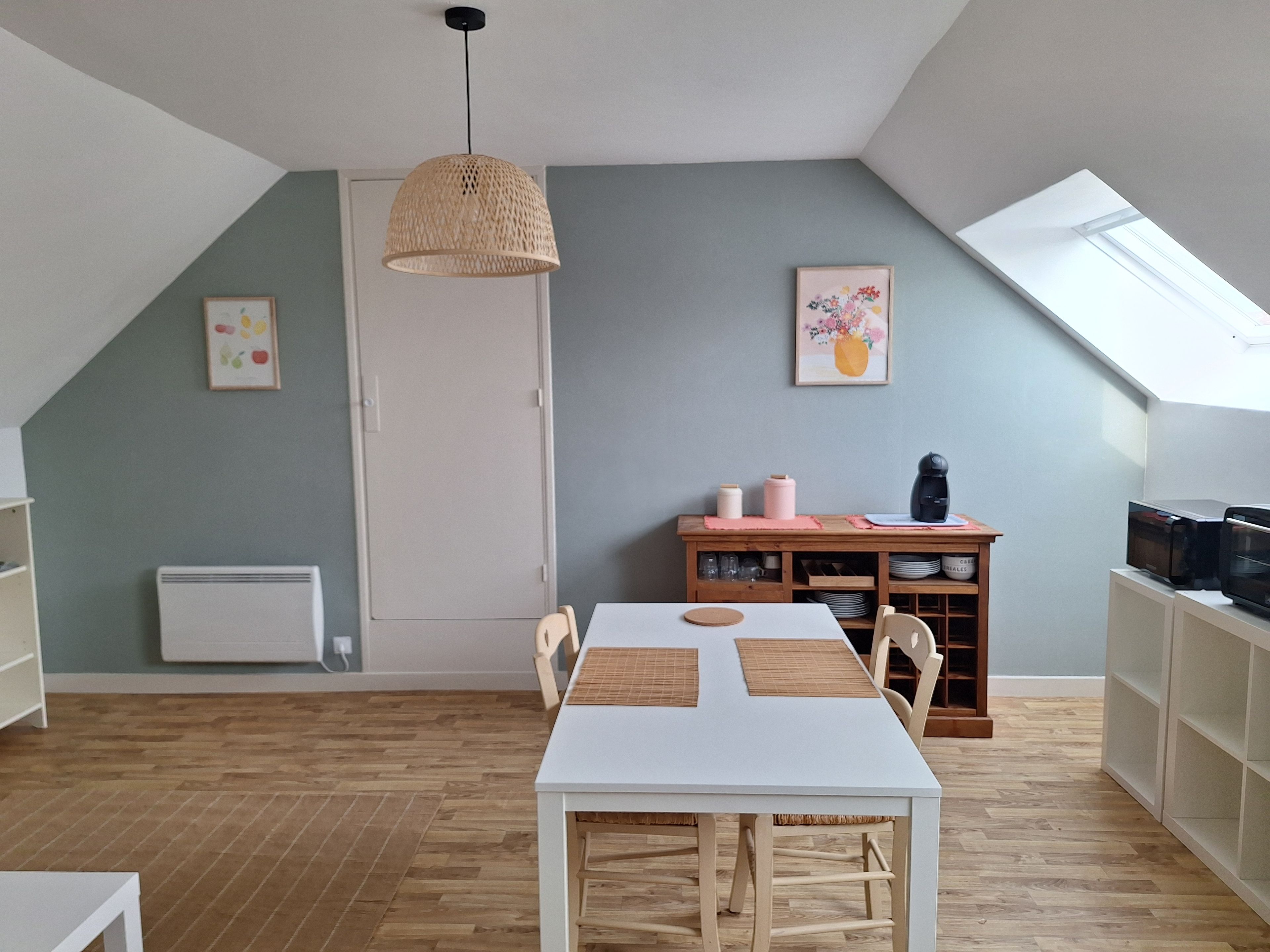 A dining area with a white table and chairs, a woven pendant light, a cabinet with dishes, and a radiator on the wall.