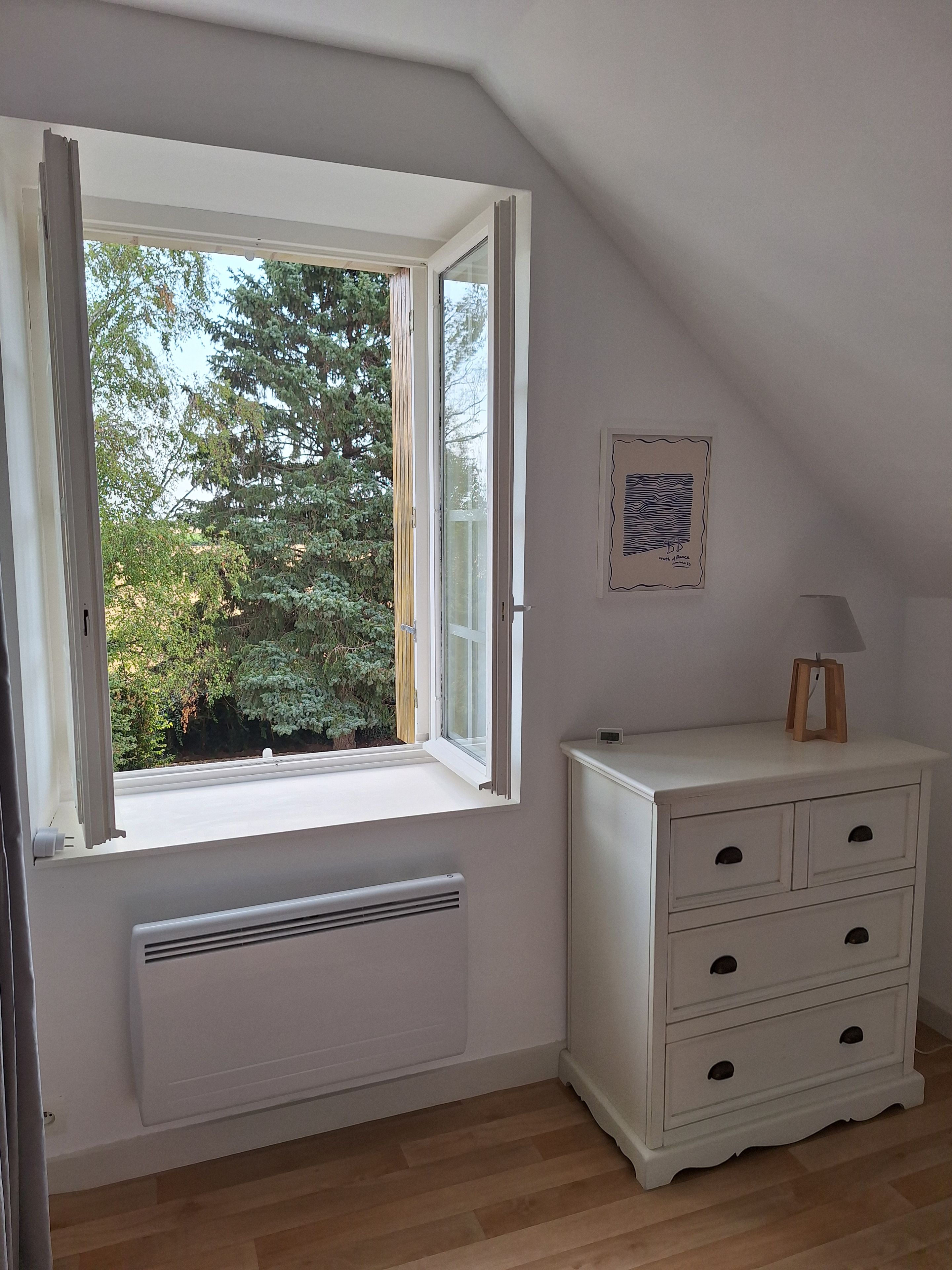 Une pièce avec une grande fenêtre, une commode blanche et un radiateur.