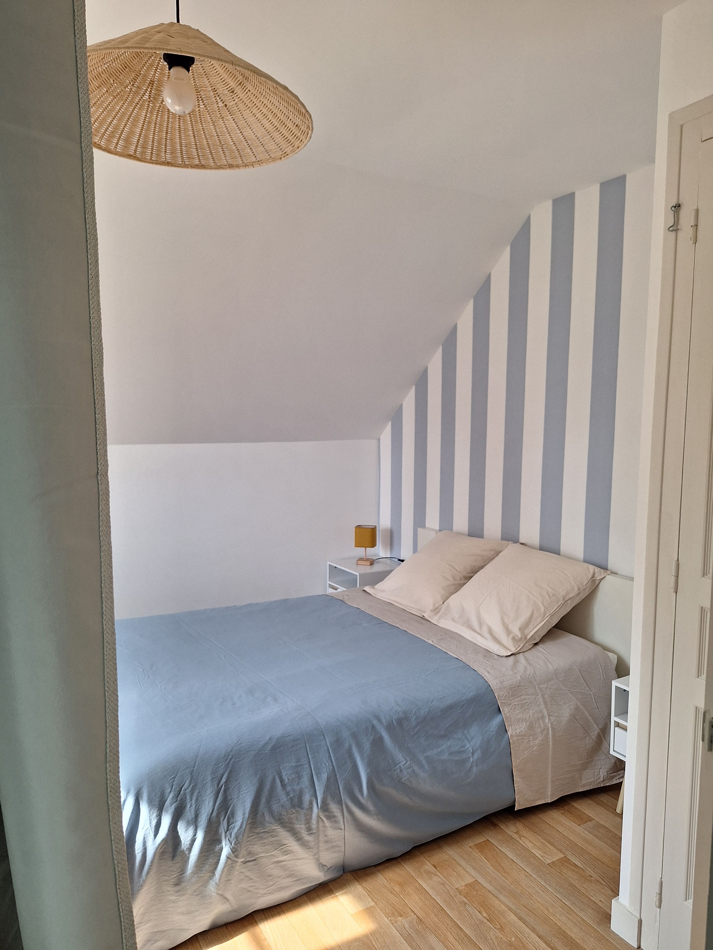 A bedroom with a bed, a bedside table, a lamp, and a striped wall.