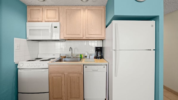 A compact kitchen with a white stove, microwave, and dishwasher, wooden cabinets, and a white refrigerator. - Barclay Towers by CoolVacay (Virginia Beach)