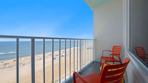 A balcony with a view of a beach and ocean. There are two orange chairs and a small table. - Barclay Towers by CoolVacay (Virginia Beach)
